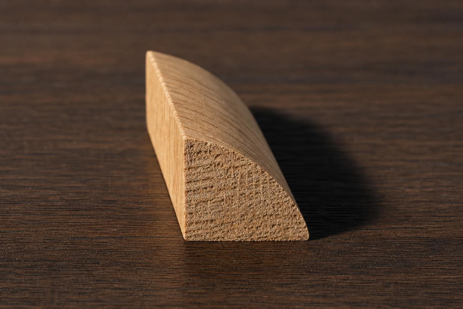 Short piece of unfinished oak quarter round seen end-on, showing its quarter-circle profile